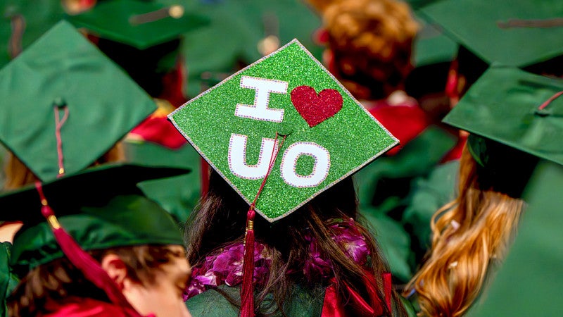 a field of green graduation caps with one in the middle that has been decorated to say "I (heart) UO"