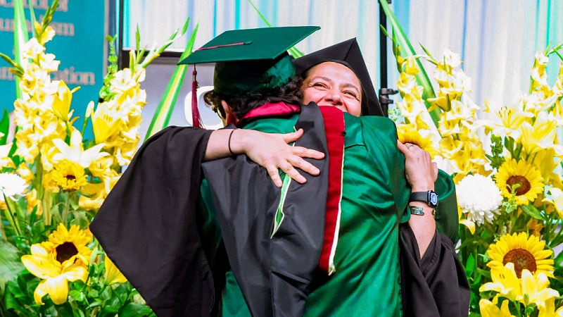 a graduating student hugs an instructor at the SOJC commencement ceremony