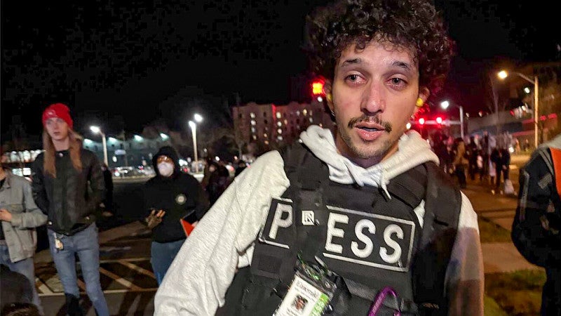 A student photographer wearing a press vest recovering from the effects of tear gas