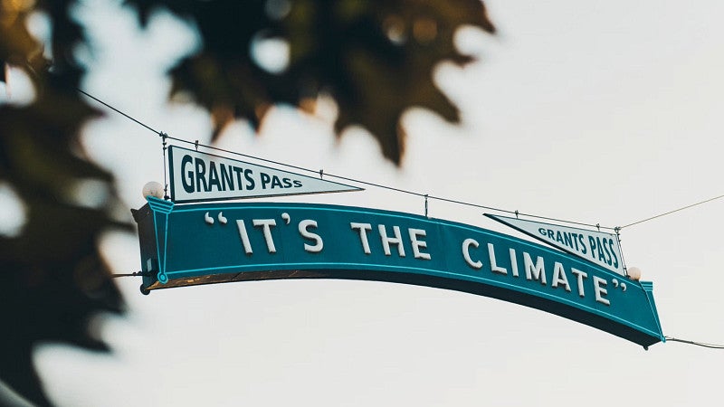 A suspended sign that says Grants Pass "It's the Climate"