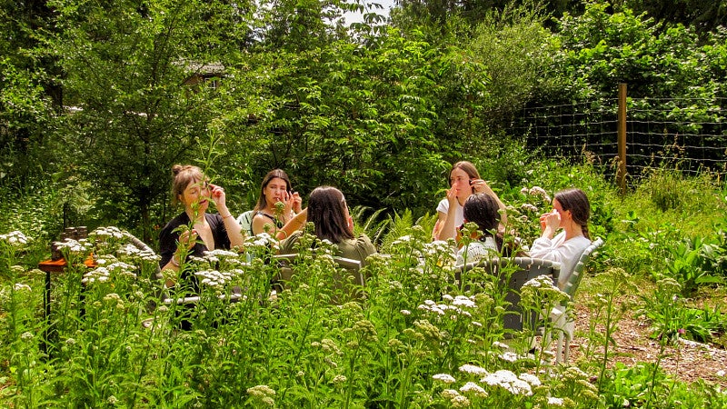 a group of women sit in the middle of a garden and use skincare