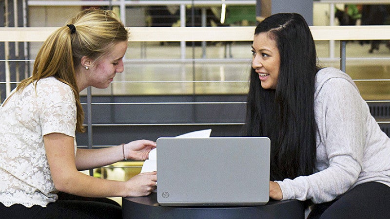 Two female students chatting while working on a computer