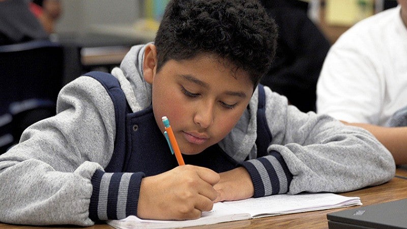 an elementary student writes using a colorful mechanical pencil