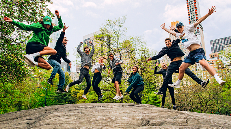 a group of UO students jump on a large rock in Central Park