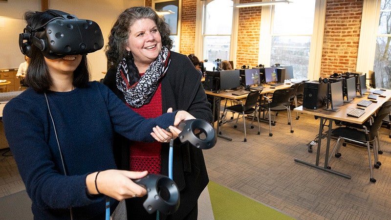 a student using a VR headset and controllers is assisted by a professor in the OR Lab