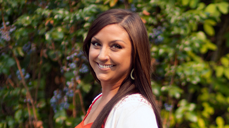 Whitney Gomes smiles while standing on a bridge in a forest