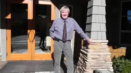 Journalism alum from 1975 Mike Mostyn poses in front of the doors of a building