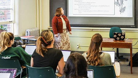 Megan Denneny stands at the front of a classroom looking at a projector screen