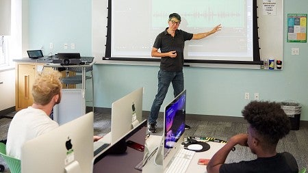 Sung Park teaches a class while gesturing to a projector screen behind him