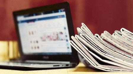 stock photo of newspapers leaning against a laptop