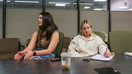 two students sit next to each other at a conference table