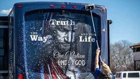 a person washes the back of a bus with a large Jesus-themed decal