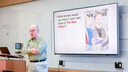 Charlie Butler stands in front of a digital screen showing a cover of The New Yorker featuring Elon Musk