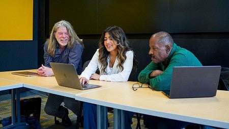 three people sitting at a table reviewing a laptop screen