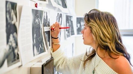 a student uses a red pen to mark up printouts of magazine spreads that are tacked on a wall