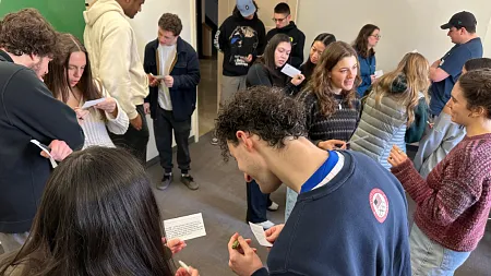 a large group of students stand discussing notes in pairs