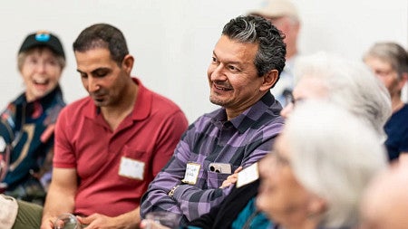 Juan-Carlos Molleda, wearing a purple and black shirt, smiles while seated amid a group of people