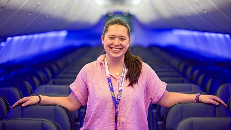 Maya Valverde poses in the aisle of an empty Alaska Airlines plane lit in vibrant blue