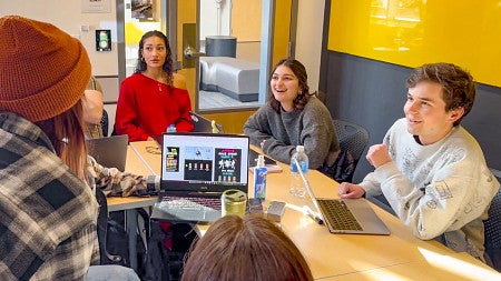 a group of SOJC students discuss creative concepts displayed on a laptop