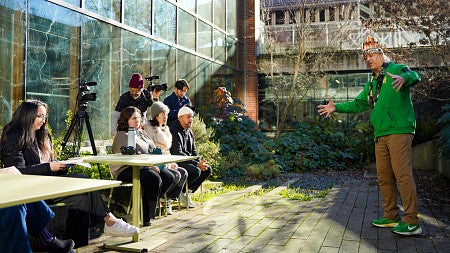 a group of people watch Jason Younker act out one of the stories of the Coquille Tribe in an outdoor courtyard
