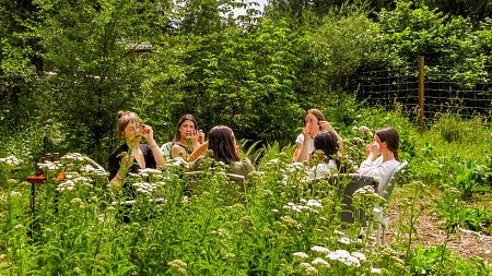 a group of women sit in the middle of a garden and use skincare