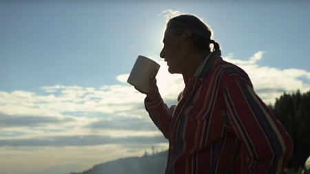 Man in stripped button-down drinks coffee as he watches the sunrise.