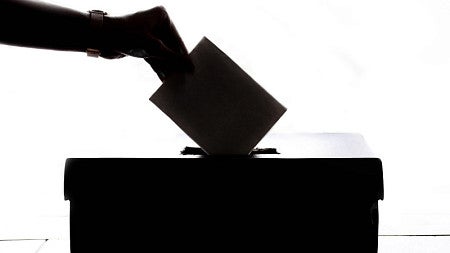Person dropping their ballot into a voting box.
