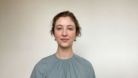 A woman wearing a light blue blouse stands for a headshot photo.