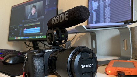 A Sony camera sits on a desk in front of a computer screen showing the video editing process.