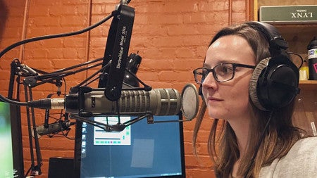 Kelly Kenoyer sits in front of a mic in a podcast studio with headphones on. 