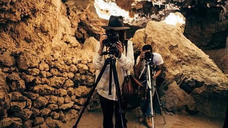Two photojournalists in a cave point their cameras toward the screen to take a picture.