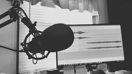 Black and white photo of a podcast microphone in front of a computer monitor measuring sound waves (Photo by Tommy Lopez)