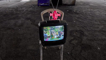 A TV sits on a plastic chair outside.