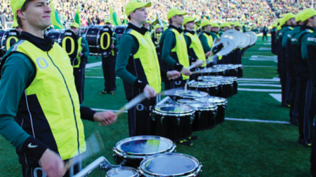 The drummers of the Oregon marching band play together on a football field. 
