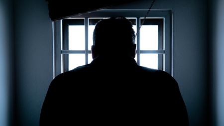 A person stands in front of a barred window so only their silhouette can be seen (photo credit - Donald Tong).