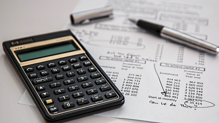A black calculator next to an open ballpoint pen on top of a spreadsheet (Photo Credit - Pixabay)