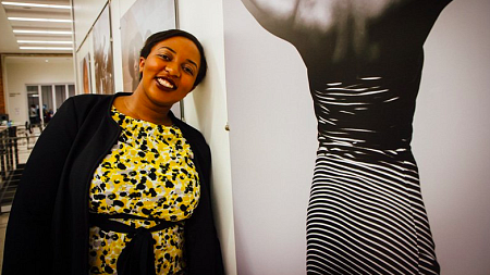 Irungu leans her head against a wall next to one of her photographs on display at an art gallery. 