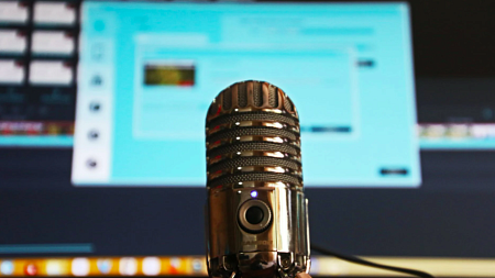 A stainless steel microphone in front of a blurry computer screen (Magda Ehlers via Pexels).