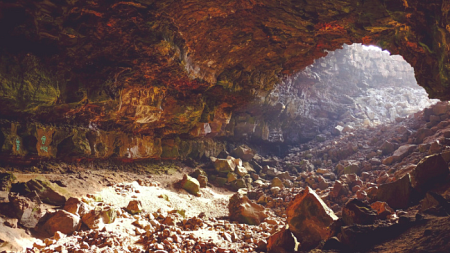Light shines in from the opening of a cave, illuminating the rock walls inside (By Free-Photos from Pixabay).