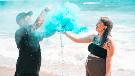 A couple standing next to the ocean pop a ballon to reveal the gender of their baby (By Alex Hussein from Pexels).