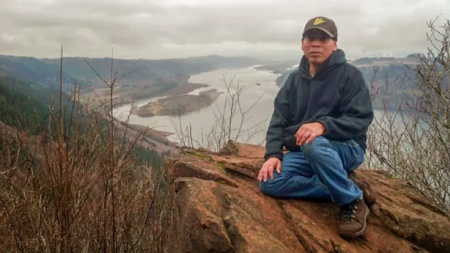 Greg Archuleta, a member of the Confederated Tribes of Grand Ronde, sits on a rock overlooking a river. 