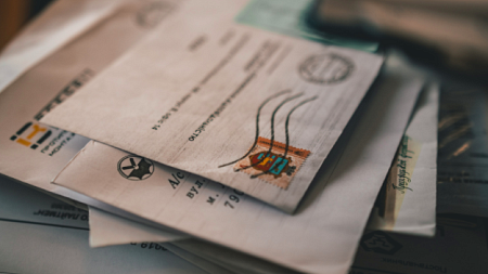 A pile of addressed and stamped letters sits on a desk on top of other paperwork (By Roman Koval from Pexels).