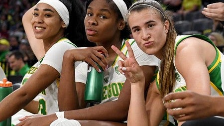 Three women basketball players pose for the camera while sitting on the bench.