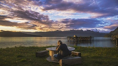 A student sitting at a wooden table looking out over a lake at sunset