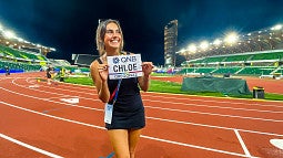 Chloe Montague holds up a track bib with her name on it while standing on Hayward Field at night