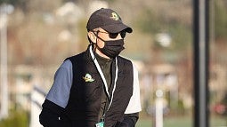 Tim Gleason, looks out at a University of Oregon athletic field, wearing a black ball cap and black face mask. 