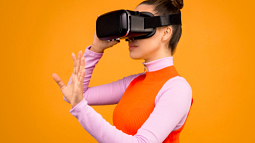 A person wearing a pink and orange outfit adjusts the virtual reality headset over their eyes (By Sound On from Pexels).