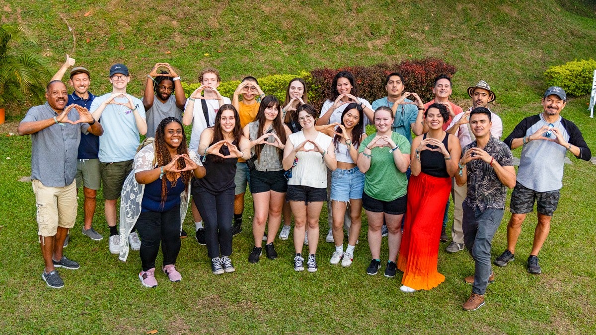 a group of people pose and make O shapes with their hands on a green lawn