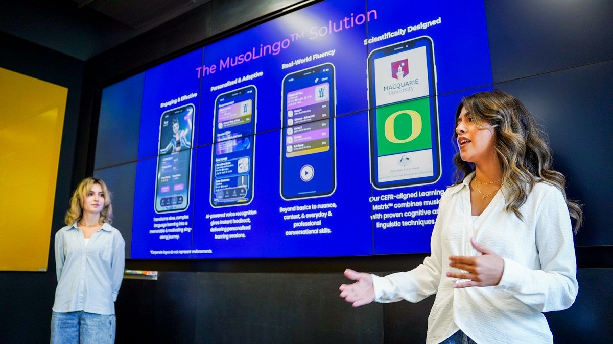two students present a project proposal in front of a large digital screen
