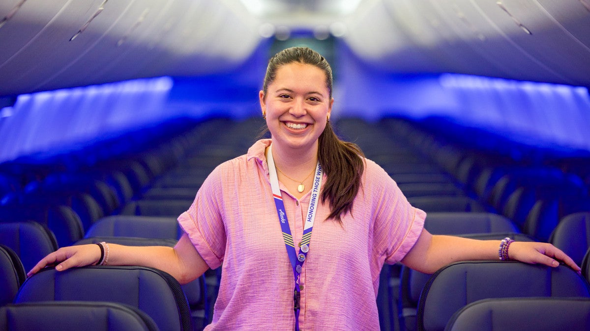Maya Valverde poses in the aisle of an empty Alaska Airlines plane lit in vibrant blue
